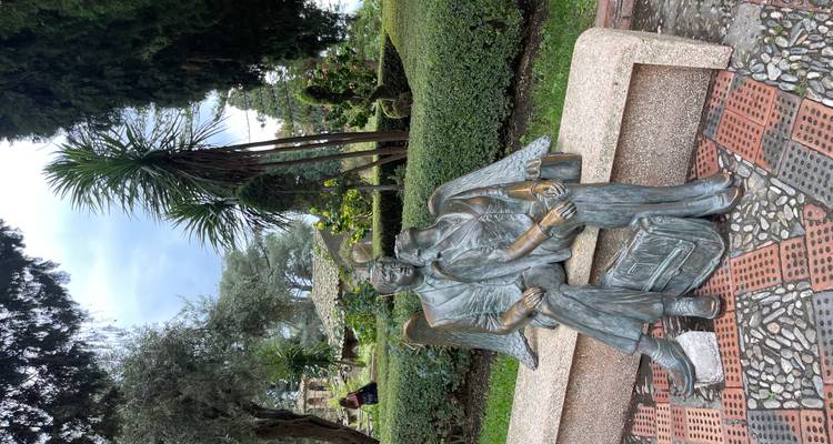 Jardin verdoyant avec haies et palmiers présentant une statue de bronze d'un couple angélique assis sur un banc de pierre.