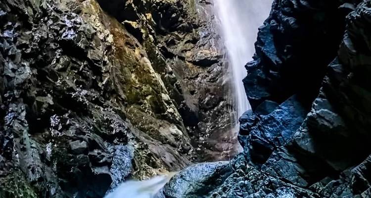 Dramatic waterfall plunges down dark volcanic rock walls into a narrow canyon.