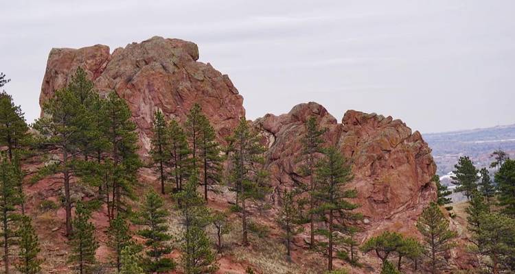 Rugged red sandstone ridge dotted with pine trees under an overcast sky in Colorado foothills.
