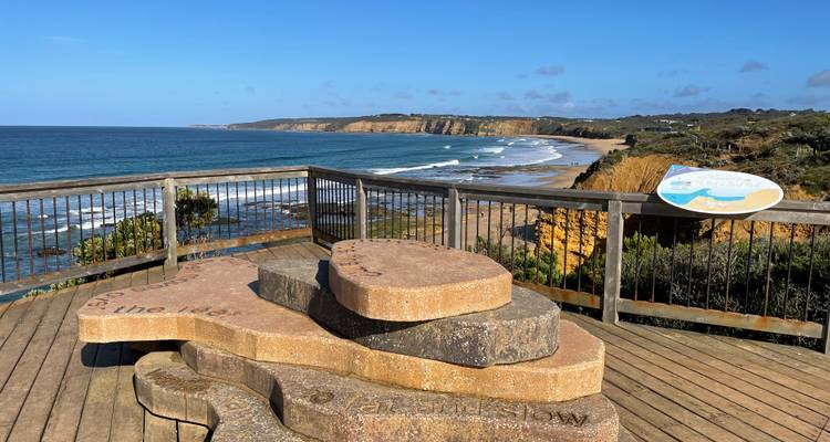 Un belvédère en bois orné de pièces sculpturales en pierre surplombe une vaste plage de surf et des falaises de grès.