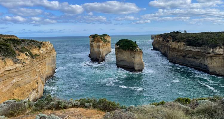 Vue spectaculaire de deux formations calcaires jumelées et de falaises abruptes s'élevant des eaux turquoise le long d'une côte sauvage.