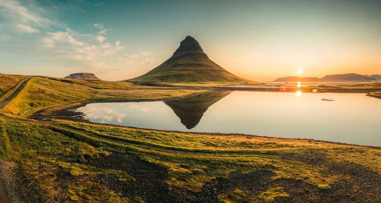 La montagne emblématique de Kirkjufell se reflétant parfaitement dans un lac calme au lever du soleil doré.