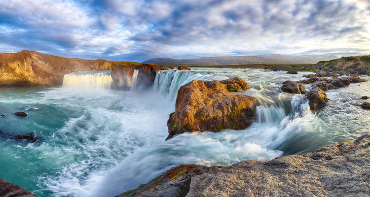 Vue panoramique d'une puissante cascade se déversant sur des roches de basalte dans un bassin turquoise.