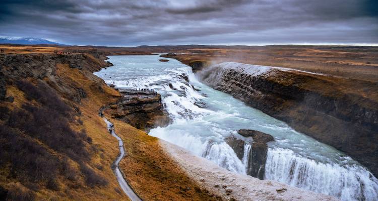 La majestueuse cascade multi-étages de Gullfoss creusant un canyon escarpé sous un ciel menaçant.