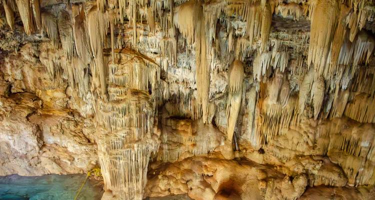 Close-up van gele druipsteen formaties die boven een turkoois cenote meer in een grot hangen
