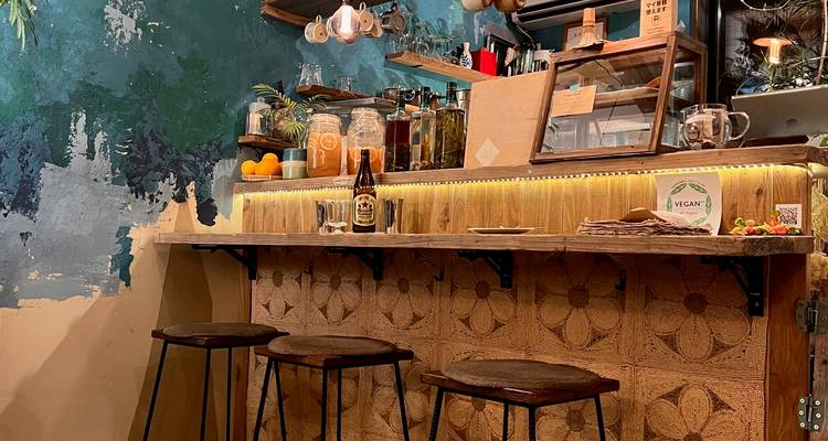 Warm, artistiek veganistisch cafeinterieur met houten bar, krukken en eclectische inrichting.