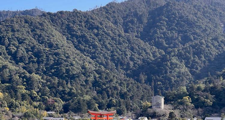 Afgelegen uitzicht op het zwevende torii van Miyajima tegen bosrijke bergen.