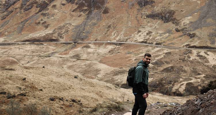 Jeune randonneur avec sac à dos souriant sur un sentier rocheux des Highlands
