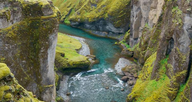 Emerald river winding through the steep mossy walls of Fjadrargljufur canyon.