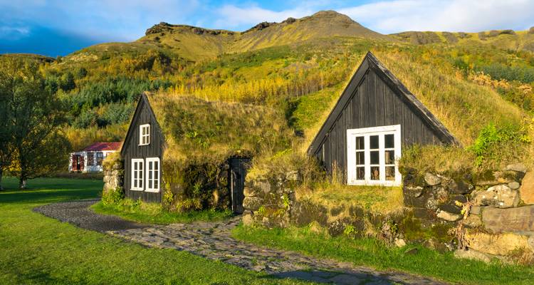 Charming black-wood turf cottages with grass roofs set against autumnal hills and evening light.