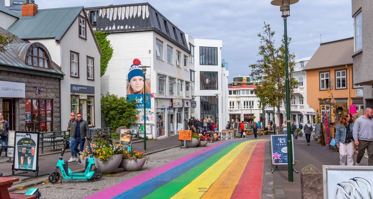 Colorful rainbow-painted pedestrian street lined with shops, cafes, and strolling visitors in downtown Reykjavik.
