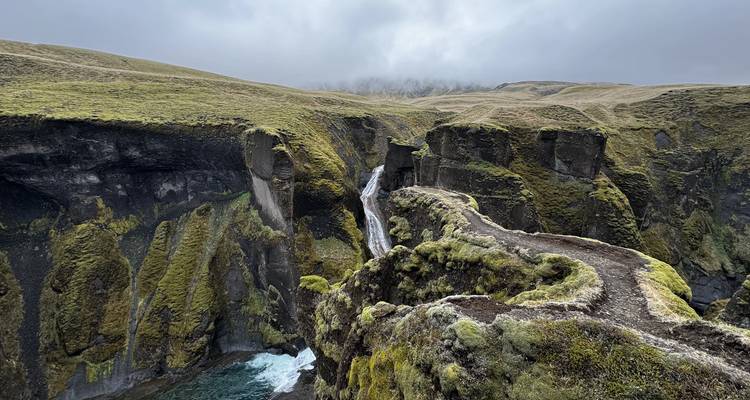 Canyon moussu spectaculaire avec une cascade étroite se précipitant à côté d'un sentier sinueux au sommet des falaises.