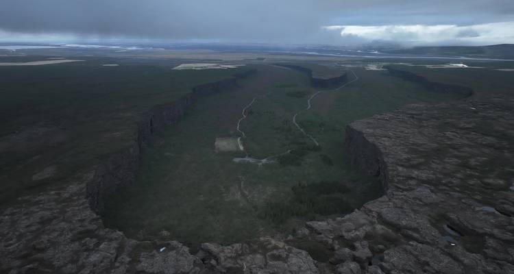 Vue aérienne d'une vaste vallée de rift bordée par des falaises hautes sous des nuages bas et sombres.