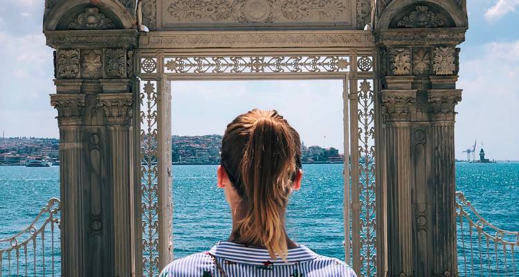 Une femme se tient devant une porte ornementale en bord de mer et regarde le Bosphore par une belle journée à Istanbul.
