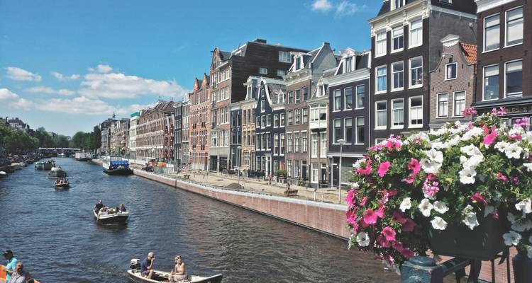 Des maisons de canal classiques bordent une voie navigable ensoleillée d'Amsterdam tandis que de petits bateaux passent en croisière.