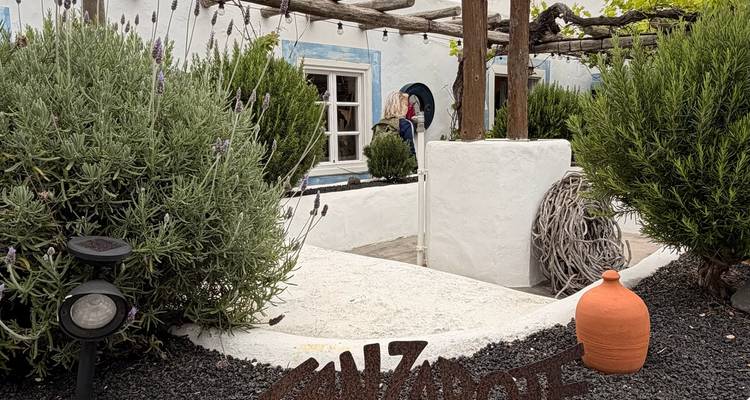 Une charmante cour blanchie à la chaux avec des buissons de lavande, une pergola en bois rustique et une petite pancarte indiquant Lanzarote.