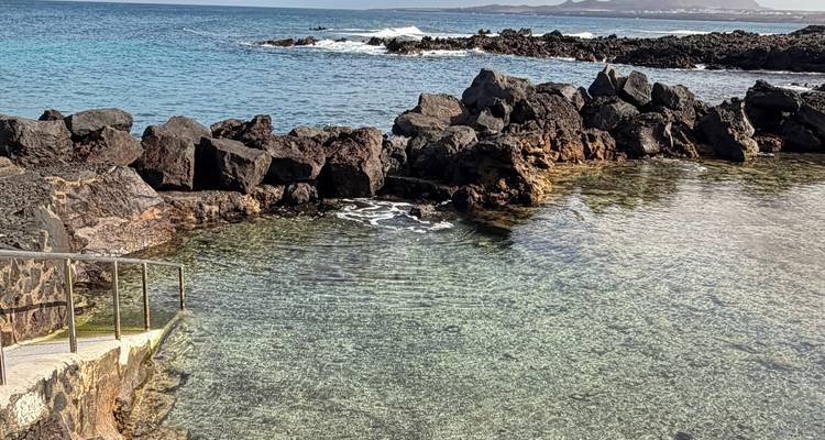 Piscina de marea cristalina rodeada de rocas de lava negra dentada y vistas al mar abierto.