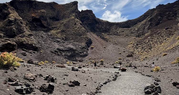 Un sendero de grava serpentea a través de un dramático anfiteatro volcánico con senderistas a lo lejos.