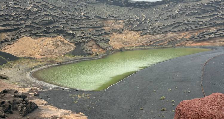 La impresionante laguna verde de El Golfo con sus acantilados volcánicos de capas negras y rojas de fondo.
