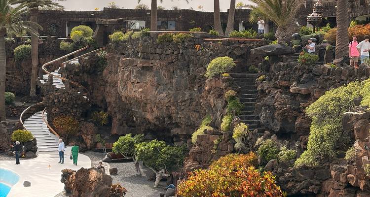 Jardines volcánicos en terrazas con plantas exuberantes, escaleras de piedra y visitantes explorando el sitio.