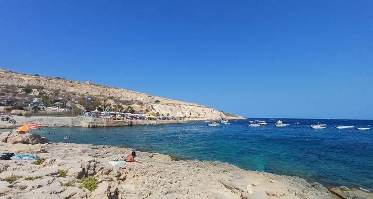 Petite crique rocheuse avec parasols, baigneurs et petits bateaux dans une eau d'un bleu éclatant.