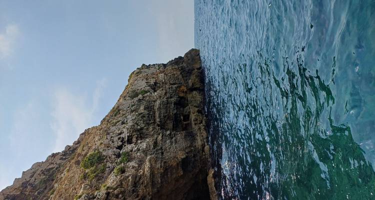 Falaise rocheuse abrupte rencontrant la Méditerranée d'un bleu profond sous un ciel dégagé.