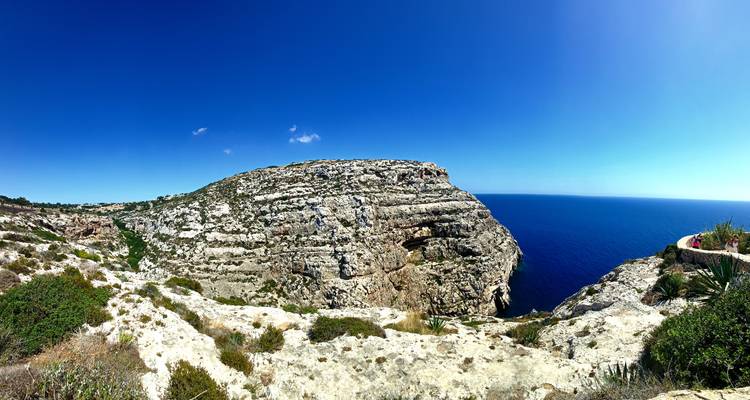 Large panorama de falaise calcaire striée s'avançant dans une mer d'un bleu intense sous un ciel sans nuages.