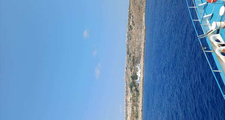 Vue depuis le pont d'un bateau peint en bleu regardant vers un rivage maltais stérile à travers une eau calme.