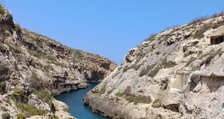 Petite baie turquoise creusée entre des falaises calcaires pâles sous des ciels d'un bleu éclatant.
