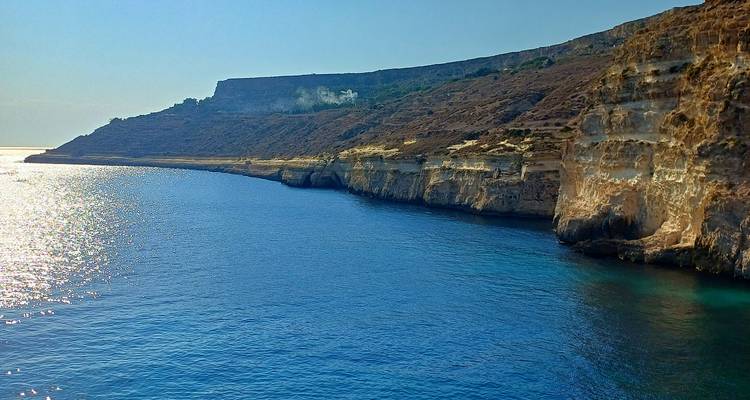 Mer ensoleillée léchant des falaises dorées escarpées et une côte de plateau lointaine.
