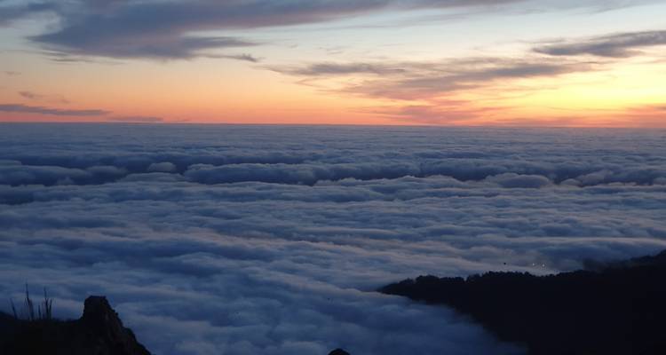 Een adembenemend bergpunt boven een dichte zee van wolken met een kleurrijke zonsonderganghemel.