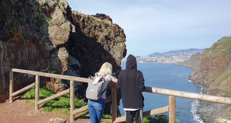 Dos visitantes se recuestan en una barandilla de madera disfrutando de las vistas panorámicas de la costa desde un mirador en un acantilado.