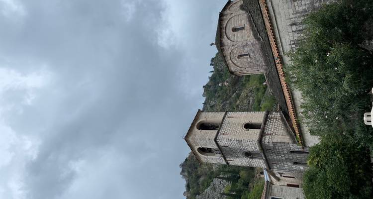 Iglesia de piedra antigua y campanario recortados contra una ladera y un cielo gris dramático