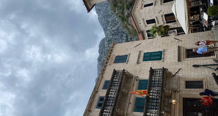 Edificios históricos de piedra en una plaza del pueblo con una bandera nacional y algunos visitantes
