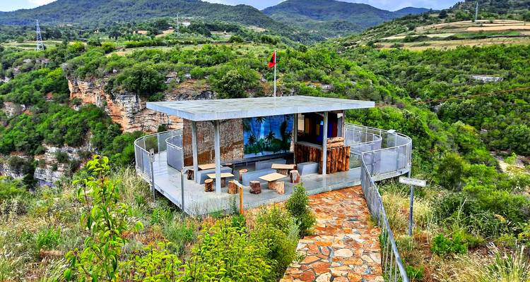 Small cliff-top café terrace overlooking dramatic green canyon landscape.