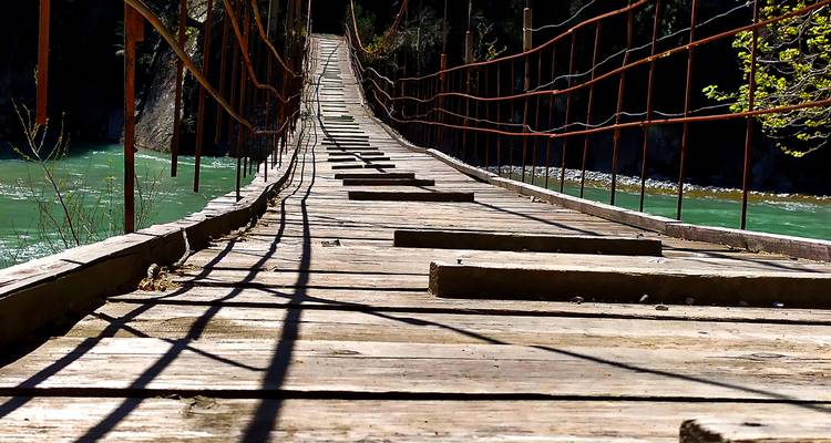 Long wooden suspension bridge stretching over turquoise river captured from low angle.