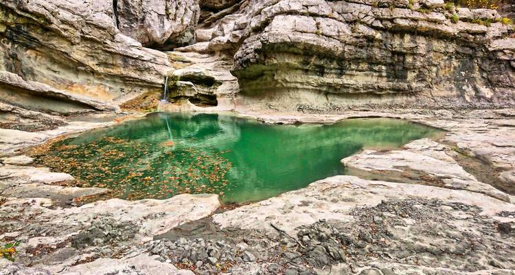Clear emerald pool nestled in sculpted limestone rock with small waterfall inlet.