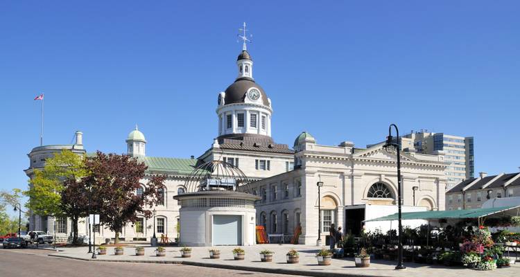 Bâtiment historique de l'hôtel de ville aux dômes avec une tour horloge sous un ciel bleu dégagé, fleurs et étals de marché au premier plan.