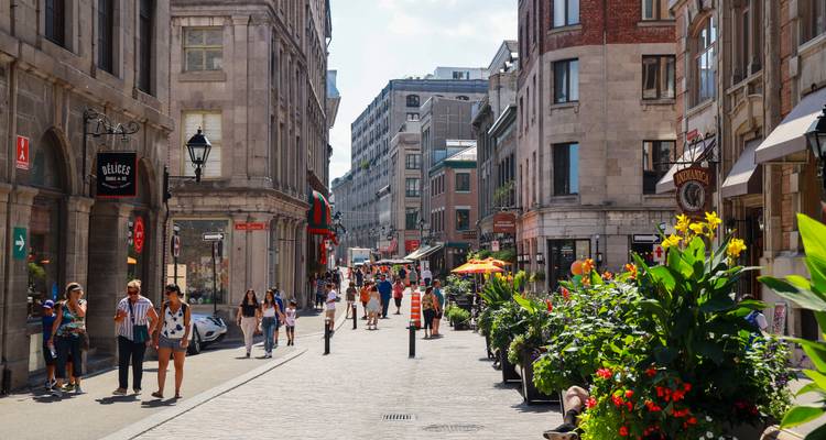 Rue pavée animée dans le Vieux-Montréal, bordée de bâtiments en pierre, de boutiques, de cafés et de fleurs colorées.