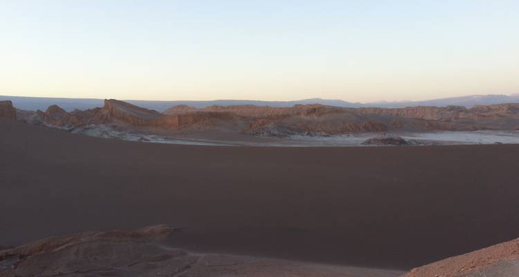 La lumière douce du soir tombe sur une vaste dune de sable sombre et des crêtes rocheuses dans la vallée du désert.