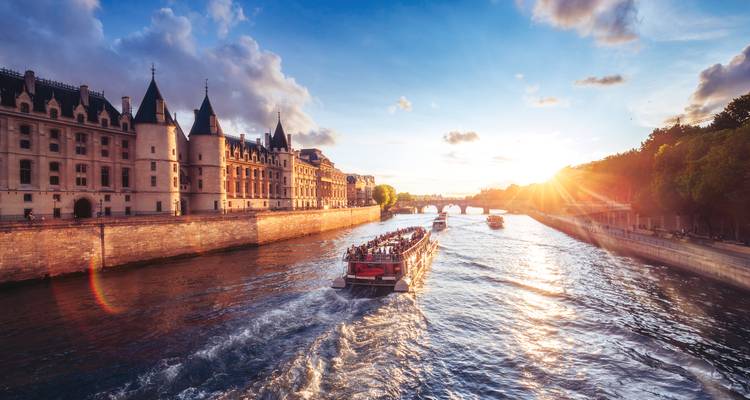 Sightseeing boat leaves a wake on the Seine at sunset beside historic Île de la Cité.