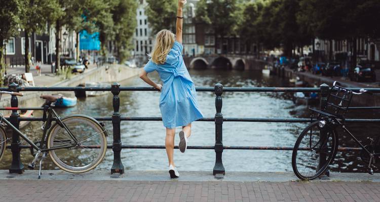 Jeune femme adoptant une pose joyeuse sur un pont d'Amsterdam surplombant un canal et des bicyclettes.
