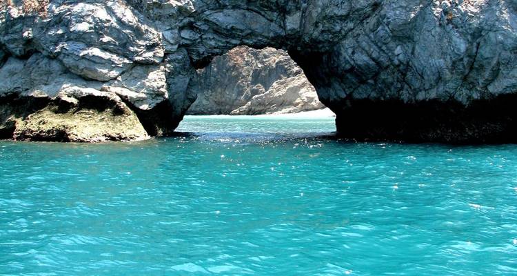 Mar turquesa enmarcado por un arco rocoso a lo largo de una costa escarpada