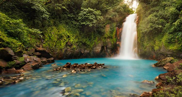 Piscina azul vibrante bajo una exuberante cascada de la selva tropical en la selva tropical de Costa Rica