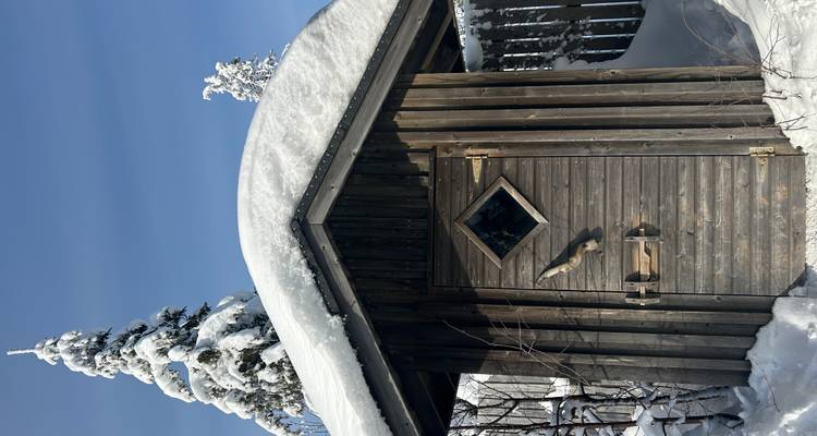 Petite cabane en bois avec de la neige épaisse accumulée sur son toit sous un soleil d'hiver brillant.