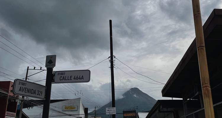 Straatborden in een klein stadje in Costa Rica met de Arenal-vulkaan die dreigend onder dramatische wolken opdoemt.