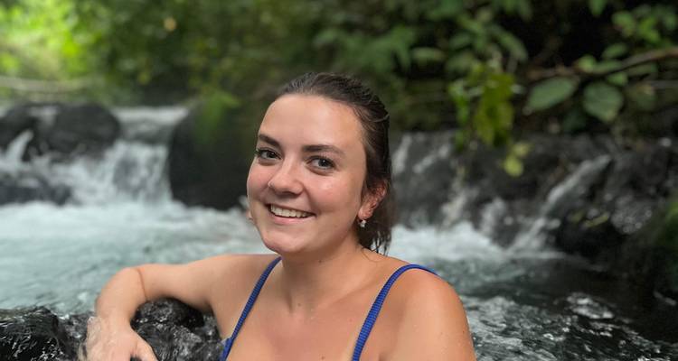 Jonge vrouw die glimlacht terwijl ze zich ontspant in een natuurlijke hete bronwateval omgeven door jungle.