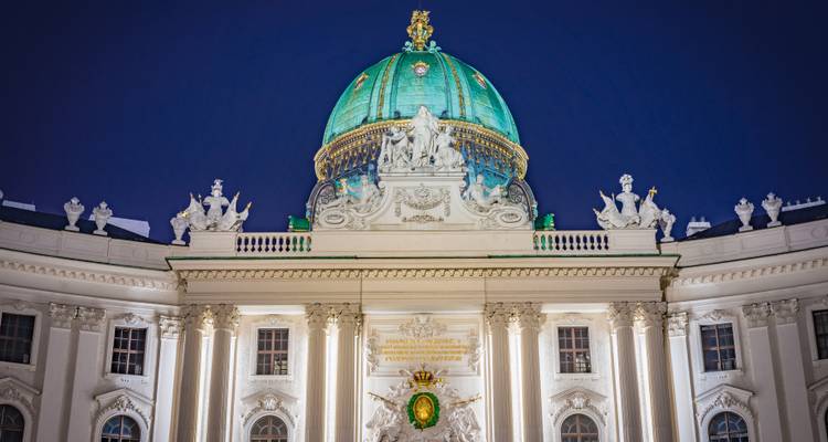 Night view of the turquoise dome and ornate façade of Vienna’s Hofburg Palace against a deep blue sky.