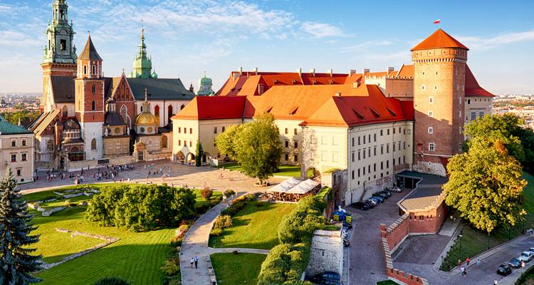 An aerial perspective of Wawel Castle’s red roofs, cathedral spires, and manicured courtyards beside the Vistula River.