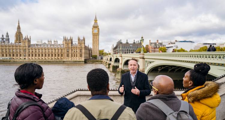 Tour guide speaks to a small group on the Thames embankment opposite the Houses of Parliament and Big Ben.